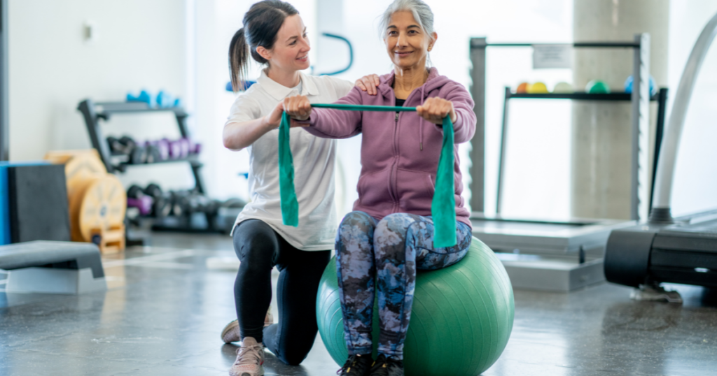 Empowering clients using education. A physiotherapist is working with a client who is sat on a balance ball and holding a resistance band