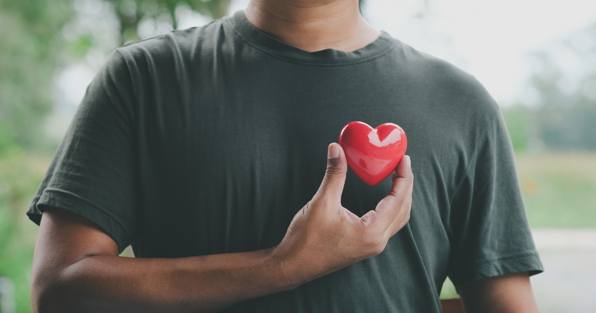 Man holding heart shape in front of chest as symbol of mental wellbeing